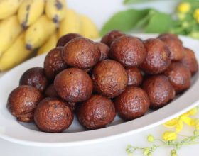 Unniyappam. Sweet rice fritters made with a batter of rice, banana, jaggery, ghee fried coconut pieces, black sesame seeds and flavored with cardamom. Shot with bananas and laburnum in the backdrop